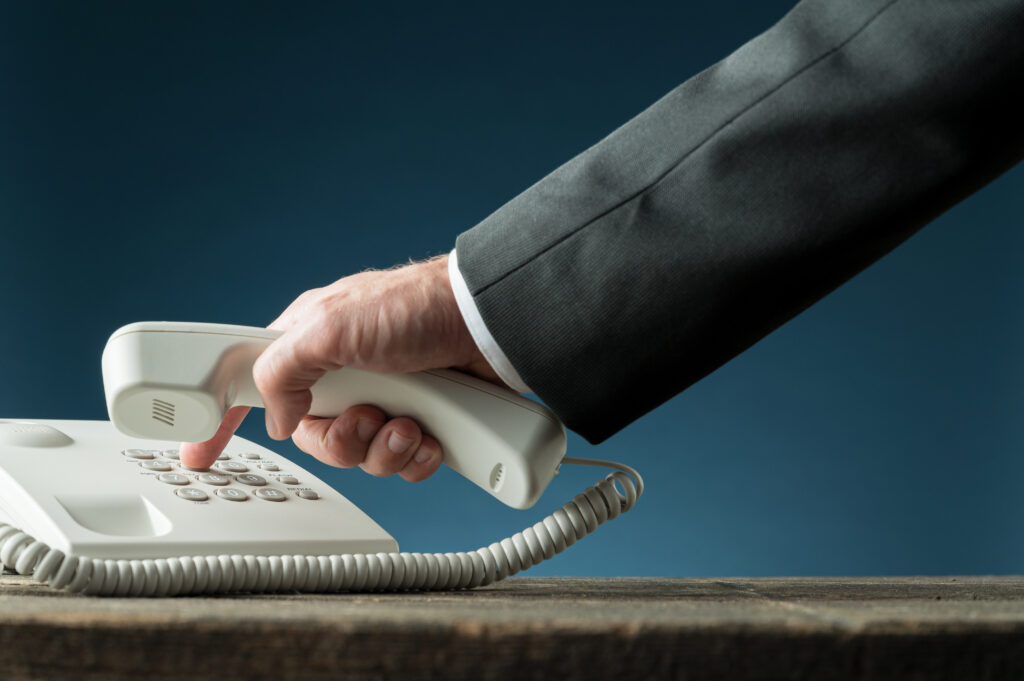 Hand of a businessman holding telephone handset dialing phone nu